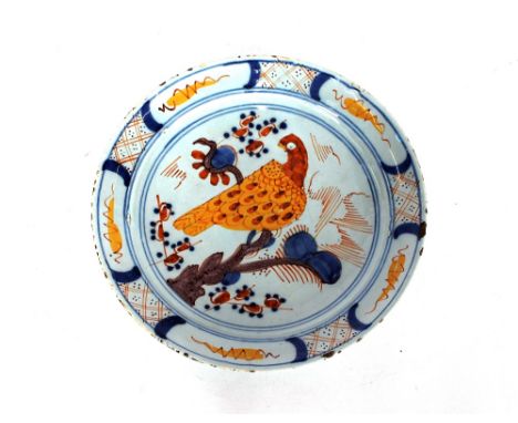 An English Delftware plate,&nbsp;painted with a large yellow stylised bird seated on a branch within blue circles and hatched