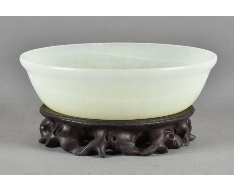 A Chinese jade brush washer, of circular form with carved rim on a hardwood base, 16 cm diameterAMENDMENT: After further exam
