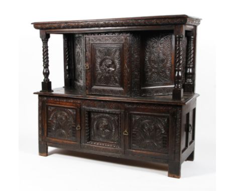 A carved oak court cupboard in the 17th century style. The canted mid-section cupboard carved with a portrait of a lady and r