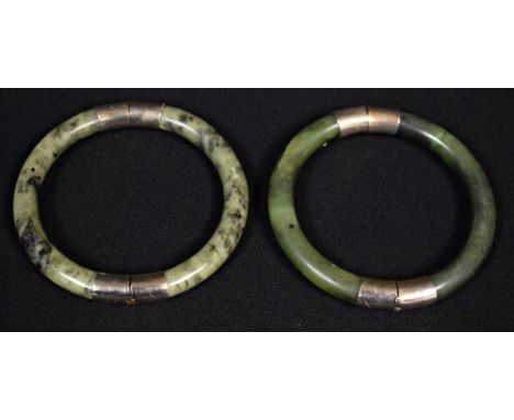 A metal mounted polished green and black spotted hardstone bangle, possibly jadite, white metal mounts; another similar (2)