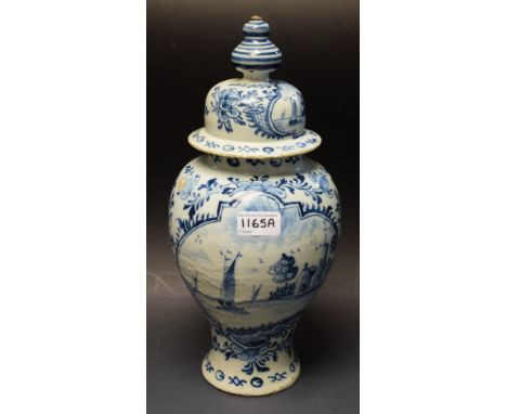 An 18th century Delft blue and white urn vase and cover, painted with boat and village cartouche within floral surround, 36.5