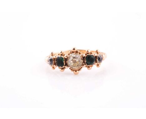 A yellow metal, diamond, and emerald ring, set with a champagne-coloured old-cut diamond, flanked with two emeralds (one rect
