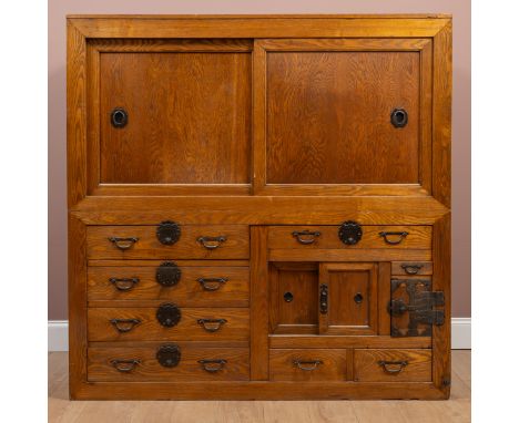The top section with a pair of panelled sliding doors raised on the bottom section of eight drawers, a sliding cupboard and a