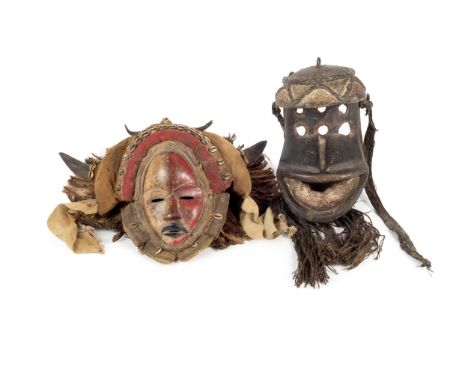 An African wood carved mask with six eyes and string beard; together with an African wood carved mask surrounded by cowrie sh