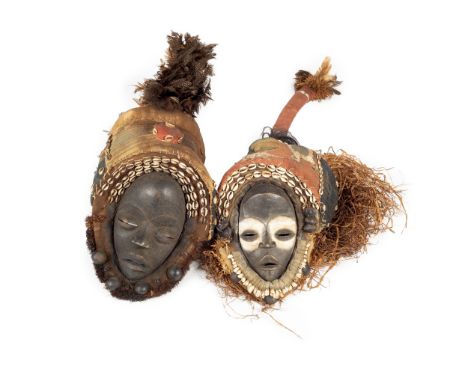 The first a Dan wood carved mask surrounded by cowrie shells and teeth decoration with grass and material embellishments; the