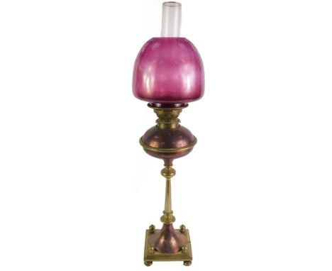 A Messenger's Patent copper and brass oil lamp, with a glass chimney and cranberry glass shade, 74cm high.