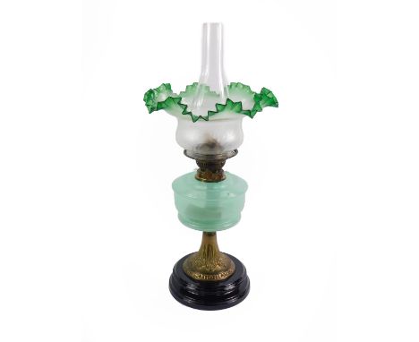 An early 20thC brass oil lamp, embossed with foliate decoration, with a light green opalescent glass reservoir,  on a black s