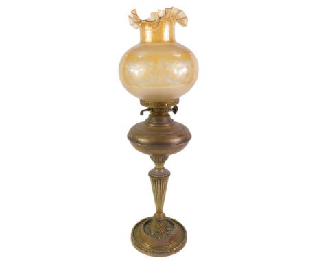 An early 20thC brass oil lamp, with a fluted stem, raised on a circular base, with an etched amber glass shade, 66.5cm high.