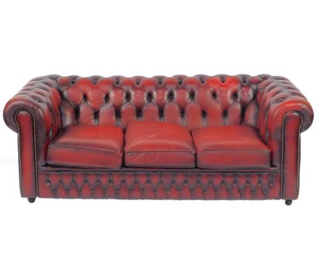 A red leather three seater Chesterfield sofa, with buttoned back and sides, three loose cushions on castors, 186cm W, 91cm D.