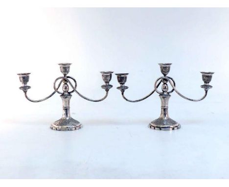 A pair of Iranian white metal (tests silver) three-light dwarf candelabra chased with geometric scrolls and foliage, 20th cen
