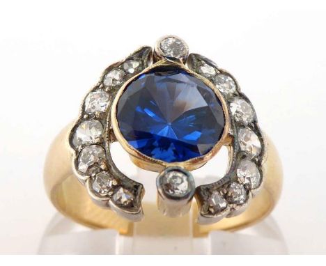 An early 20th century synthetic sapphire and diamond ring, the central round cut sapphire 8 x 4.5mm, rub over set above an ol