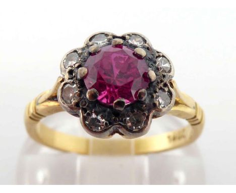 A mid 20th century synthetic ruby and diamond cluster ring, the central round cut ruby 5.4mm, in a surround of small brillian