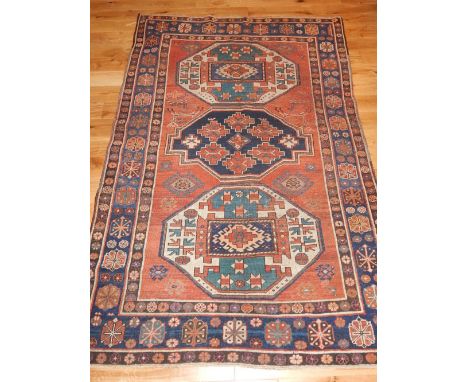 Red ground Kazak carpet, three geometric medallions to centre, the blue ground border and stylised floral design, fringed. 22