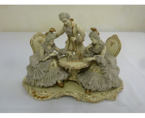 A Continental figural group of three figures playing a board game on raised shaped oval plinth, marks to the base