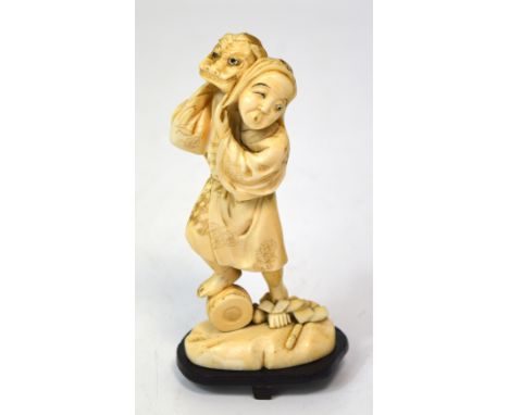 A Japanese Meiji period carved ivory okimono modelled as a two-headed figure and wearing a cloak, with shaped associated wood