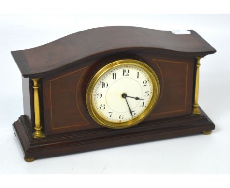An Edwardian inlaid mantel clock, dial set with Arabic numerals, flanked either side by brass pillar style supports on feet.