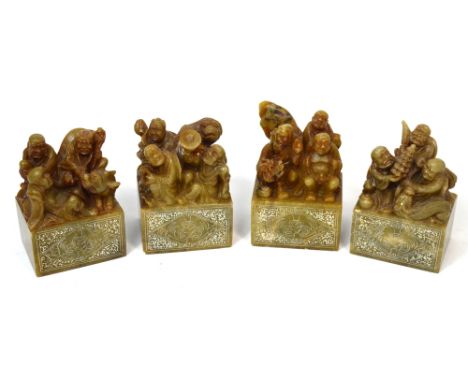 A group of four Chinese carved soapstone scroll weights, each upper section set with numerous figures and with rectangular lo