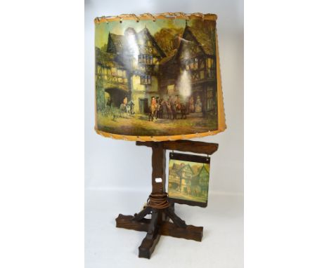 An early 20th century lamp in the style of a country public house sign topped with a paper shade decorated with hunting scene