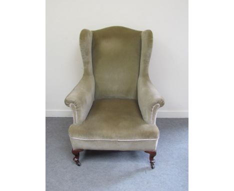 A late Victorian walnut wingback armchair, the out swept scroll arms over cabriole feet and ceramic castors united by a turne