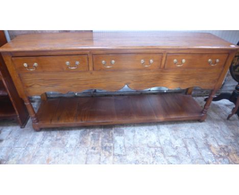 An oak pot cupboard dresser base of three drawers over shaped apron above shelf raised on turned supports - 173cm x 43cm x 83