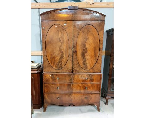 A late Georgian figured mahogany press cupboard, the upper section with arch top and 4 sliding trays enclosed by 2 oval panel