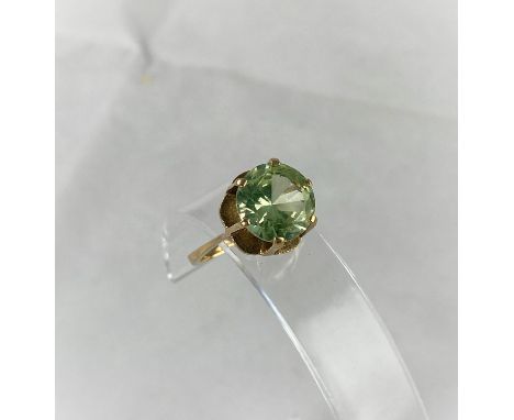 A yellow metal dress ring with citrine/peridot type stone in raised setting, tests as 9 ct, size N 