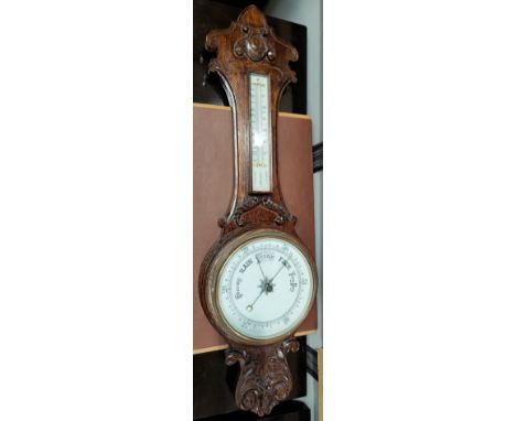 An Edwardian carved oak aneroid barometer with long thermometer box 