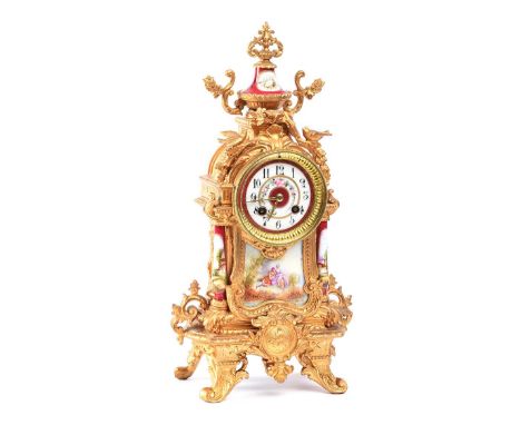 GILT METAL MANTLE CLOCK WITH PORCELAIN PANEL AND COLUMNS ON FOUR SPLAYED LEGS WITH A CIRCULAR PORCELAIN DIAL OF 4 INCHES.HEIG