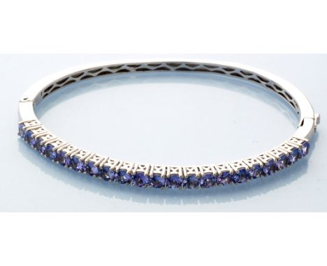 A tanzanite bangle, the twenty-one circular facet cut tanzanites within silver openwork setting and bangle, 7.8cms wide.