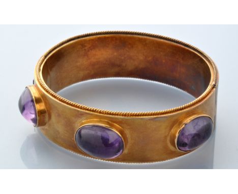 A Victorian yellow metal and paste stone bangle, the oval bangle with ropework edge, set with three oval purple glass cabocho