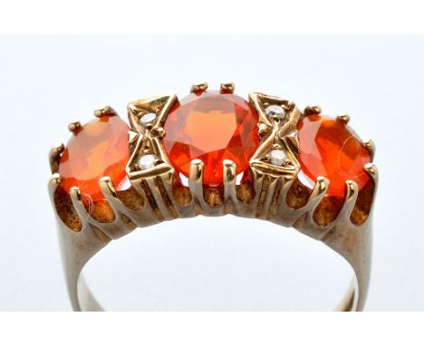 A three-stone fire opal ring, each oval facet cut fire opal separated by a pair of diamonds, in yellow metal mount, on 9ct. y