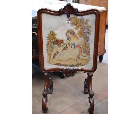 A late Victorian mahogany firescreen with a needlework scene of child and dogs in an elaborate frame and supports 