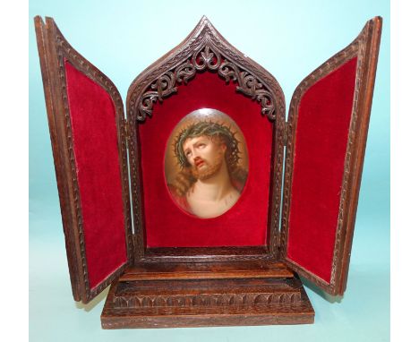 A well-carved oak icon holder in the form of a Gothic arch, the two hinged doors revealing a painted porcelain plaque depicti
