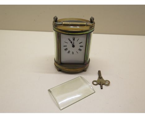 An oval brass carriage clock not currently running, front glass loose, 13cm tall with handle down 