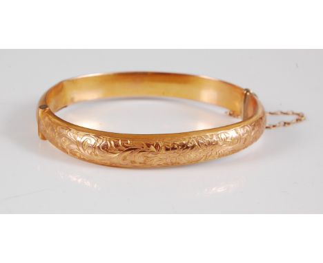 An early 20th century 9ct hinged bangle, the upper half with bright cut engraved decoration, with plain lower half, 9mm thick