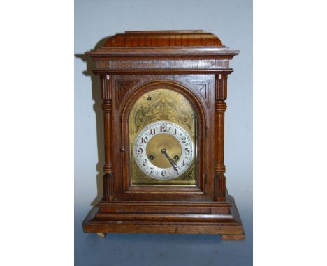 A late 19th century continental oak cased mantel clock, having engraved arched brass dial with painted chapter ring, Arabic n