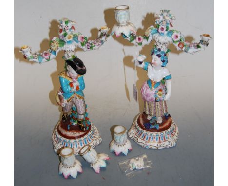 A pair of continental porcelain two-light candelabra, modelled as a young huntsman and his maiden holding aloft a bunch of gr