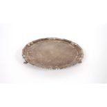 A silver card tray, having shaped border raised on three hoof feet, Sheffield 1936, 21cm dia., 254.