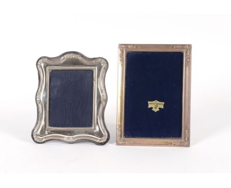 A silver mounted easel photograph frame, of cartouche shape; and an oblong similar with foliate embossed decoration&nbsp;