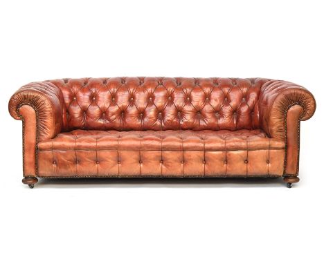 A three seater button upholstered Chesterfield sofa, in red leather, on compressed bun feet and later casters, approx. 207cm 