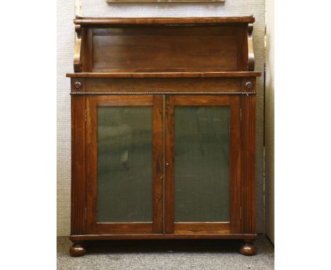 An early Victorian rosewood chiffonier, with a shelf on a pair of 'S' scroll brackets, over a pair of glazed doors and bun fe