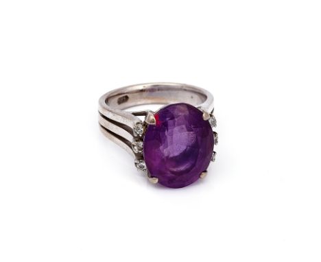 A WHITE GOLD, AMETHYST AND DIAMOND RINGClaw set with an oval cut amethyst, between circular cut diamond set three stone shoul