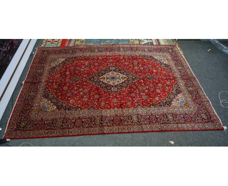 A KASHAN CARPET, PERSIANThe madder field with indigo and ivory medallion, matching spandrels all with floral sprays, a dark i