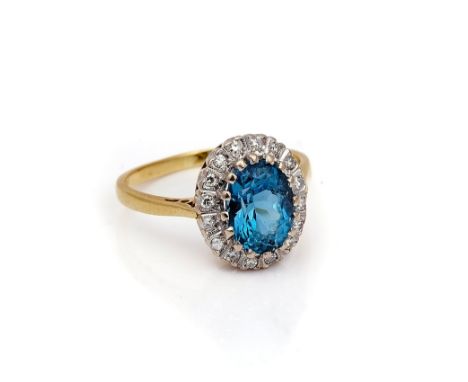 AN 18CT GOLD, BLUE TOPAZ AND DIAMOND OVAL CLUSTER RINGClaw set with the oval cut blue topaz in a surround of circular cut dia