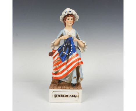 A charming decanter portraying Betsy Ross in a blue prairie dress, seated on a wooden chair while assembling the first Americ