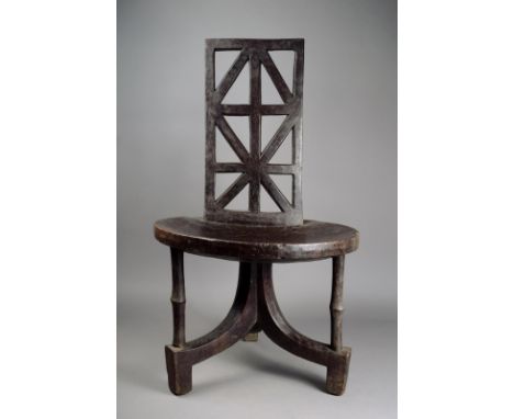 An Ethiopian chair wood, with a pierced panel back and a circular seat, on a tripod base with bar supports, 93cm high, 54.5cm