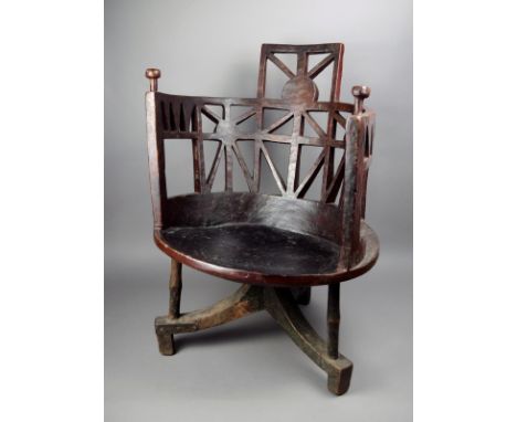An Ethiopian armchair wood, with a pierced wrap around back with two hand grips, on a tripod base with bar supports, with red