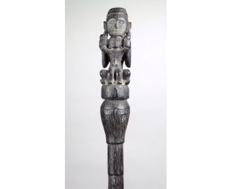 A Dayak pig trap stick Indonesia ironwood with a seated ancestor holding a male figure, with a tapering pointed end shaft, 60