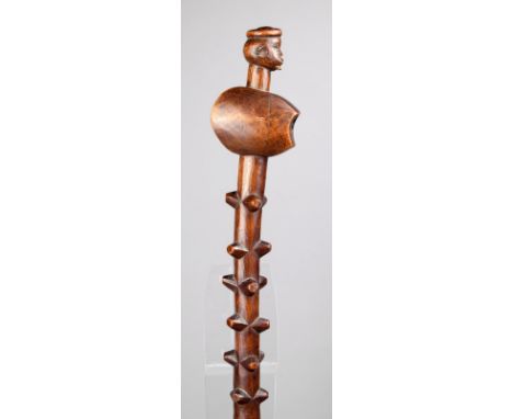 A Zulu prestige axe shaft South Africa wood, with a male head finial with a ring headdress, pointed lashes and a short beard,