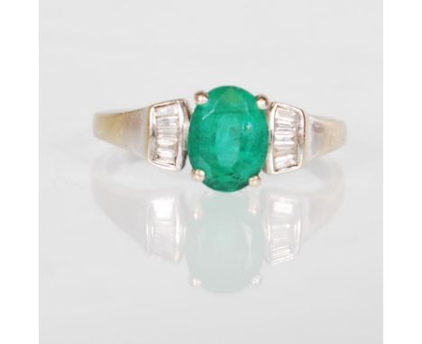 A hallmarked 18ct white gold ring set with an oval cut emerald with diamond accent stones to the shoulders. Hallmarked London